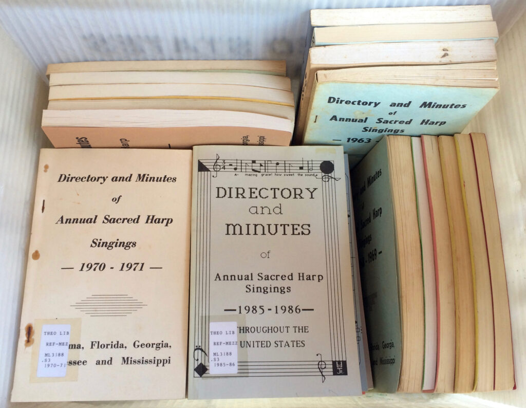 A photograph illustrating what some historical minutes books look like: a large bin containing dozens of annual volumes of the "big minutes" with colors and typography representing different historical printing technologies and styles of design.
